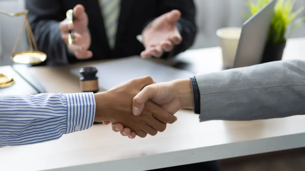 Two people shaking hands while a person in the back is facilitating.