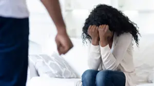 A woman cowering in fear while a person is clenching their fist.