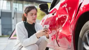 A woman looking at her phone after discovering that her car was hit.
