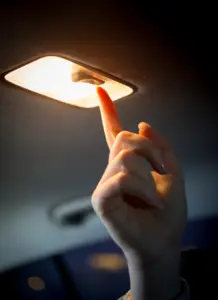 A person turning on a car's interior lights at night. 