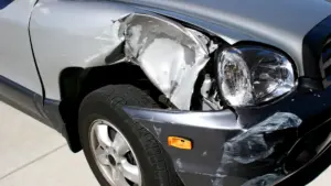 A car with a broken front headlight and bumper. 