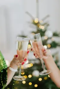 Two people clanking their glasses together in front of a Christmas tree. 